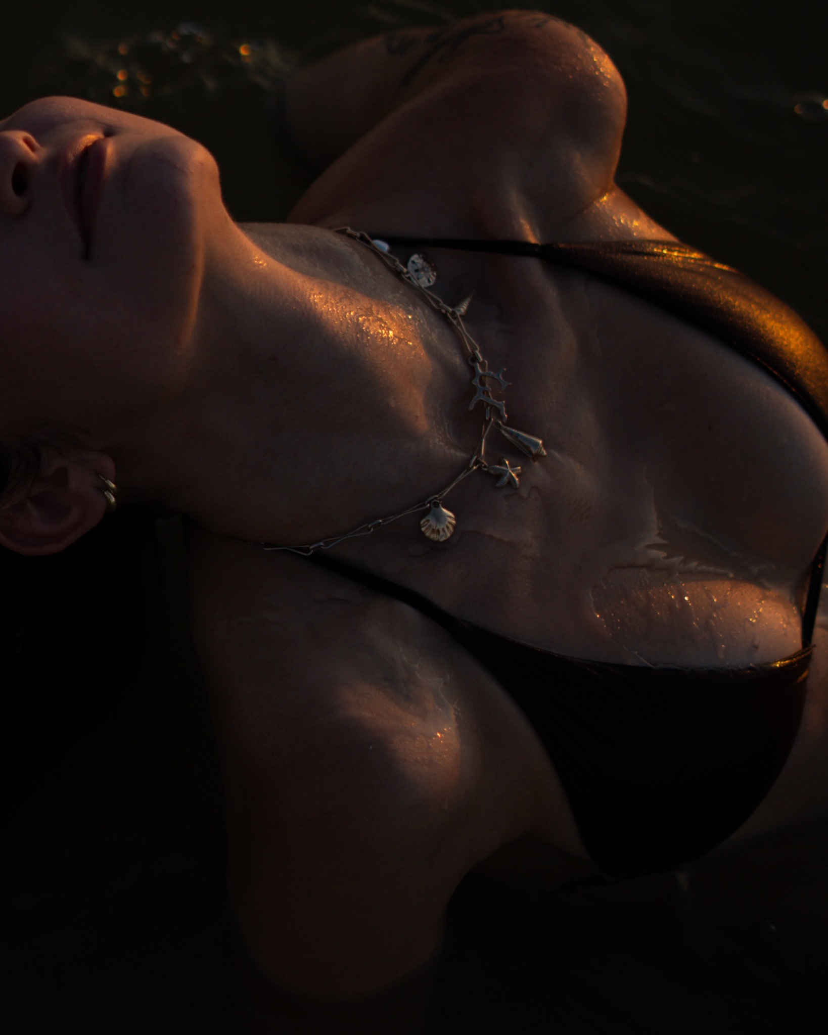 Lindy floating in dark water with warm golden reflections across her necklace and skin