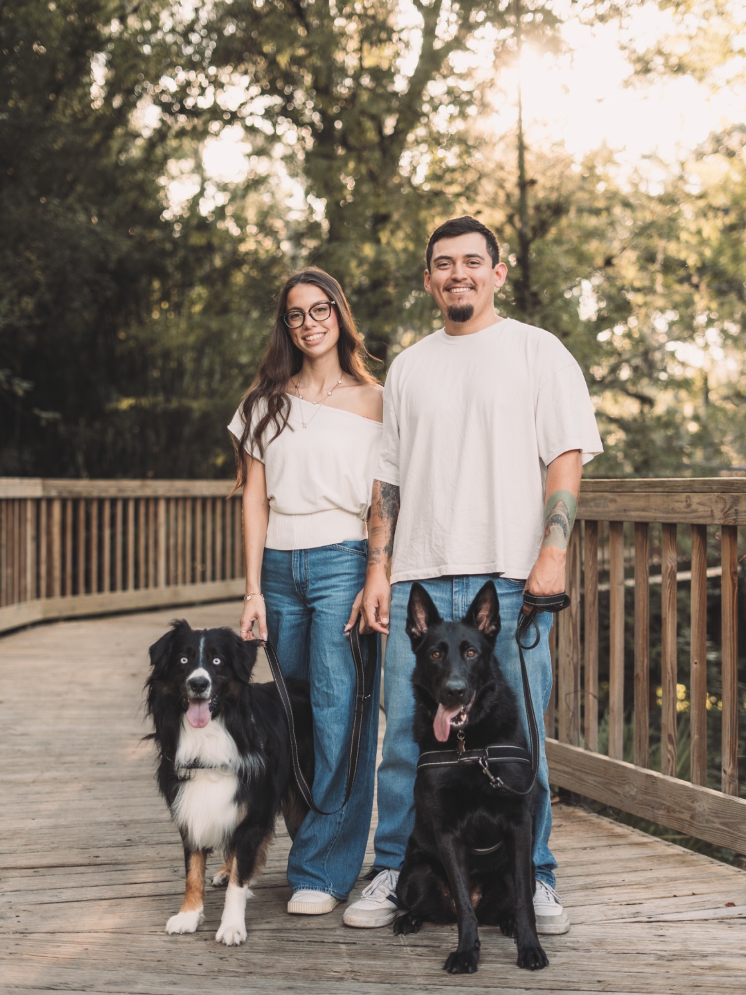 A couple with their two dogs on a sunlit wooded boardwalk