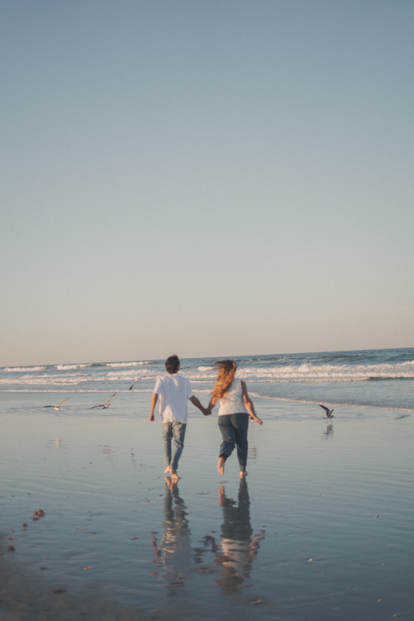 A couple walking hand in hand toward the ocean