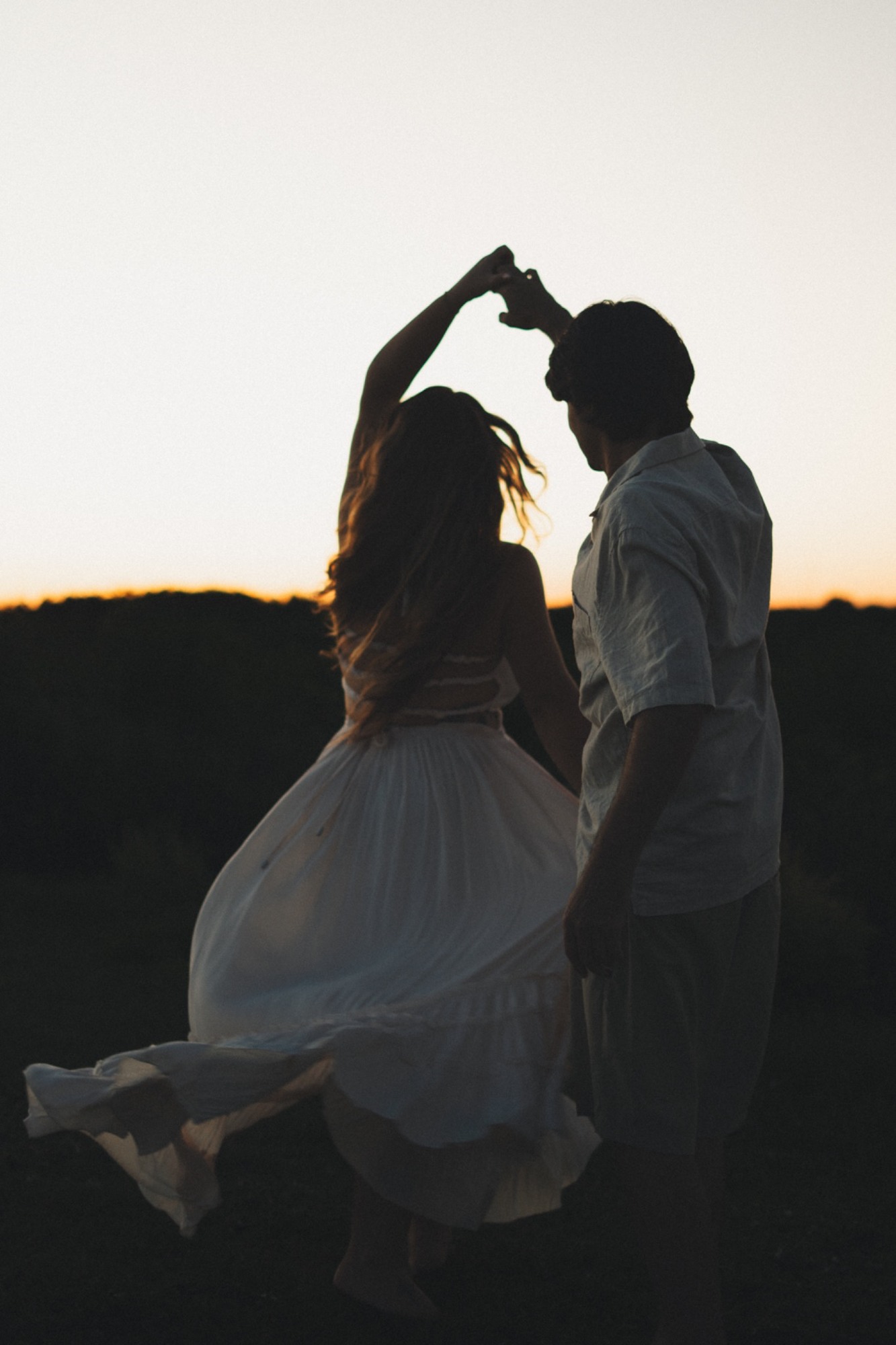 A couple twirling in silhouette against the sunset